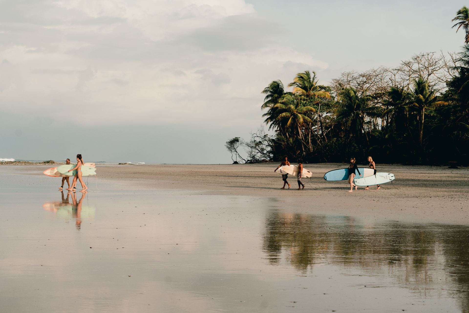 Two small groups of surfers walking across a mirror-flat, empty Santa Teresa beach at low tide